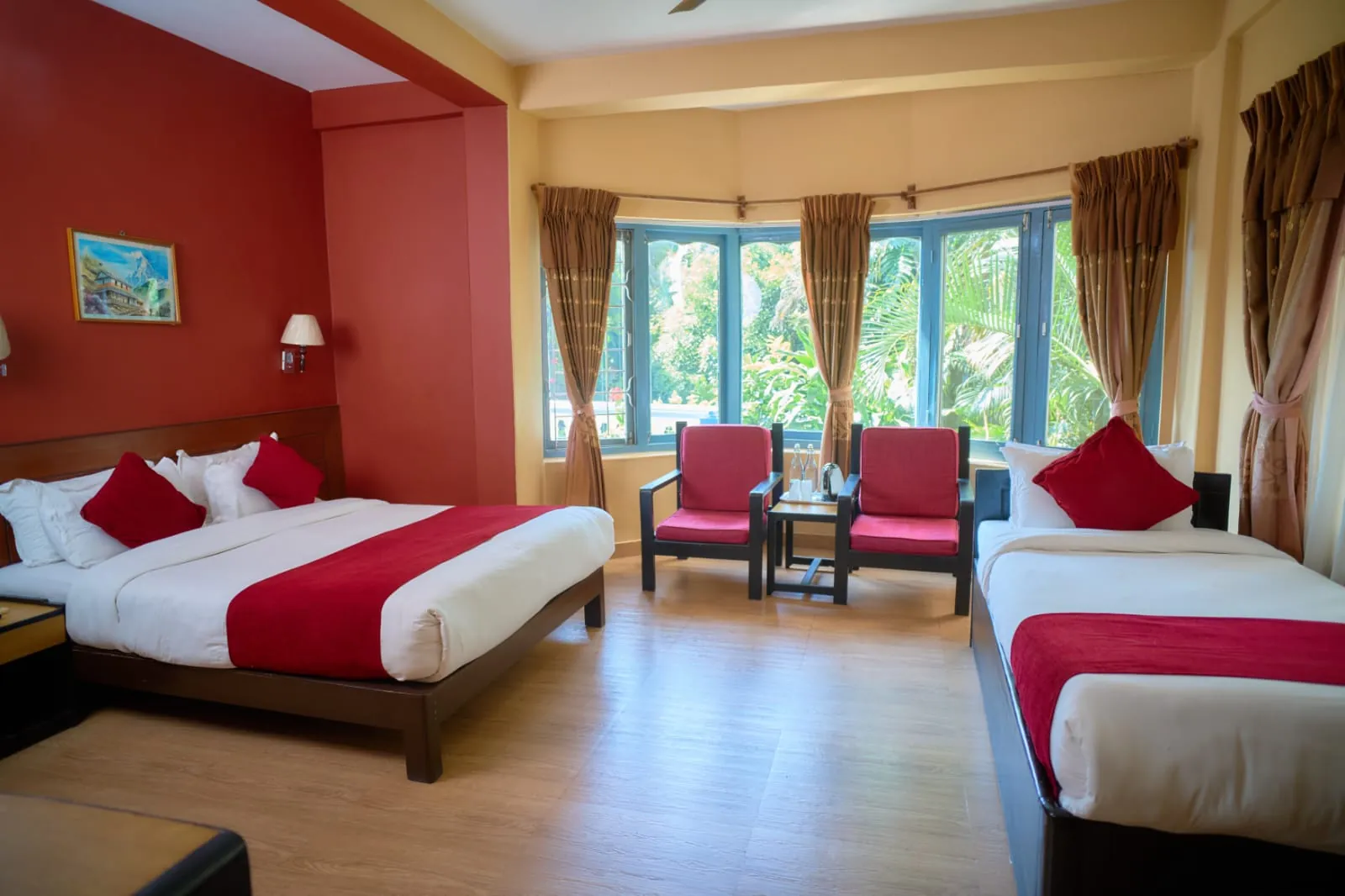 Bright deluxe room with a double and a single bed, red armchairs and garden windows