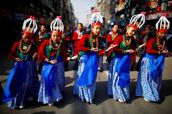 Gurung dancers in white headdresses and blue skirts in a street procession