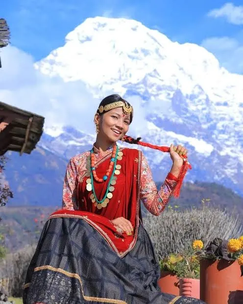 Gurung woman in red velvet blouse and coral jewellery with Annapurna South behind